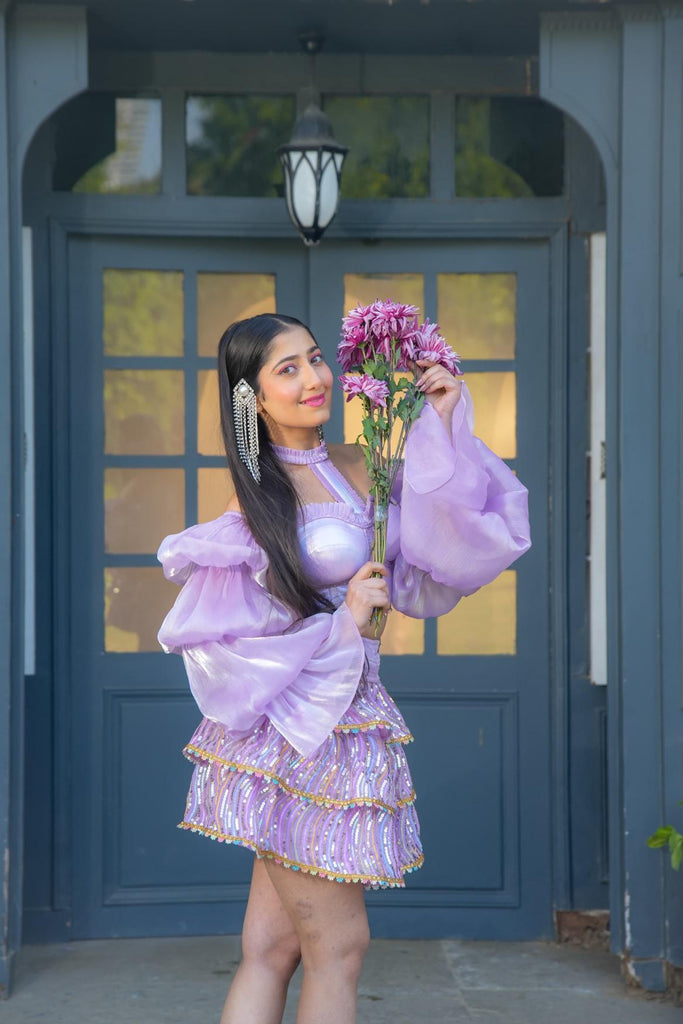 Model wearing Famameha lavender boho luxury outfit with puffed sleeves and embroidered skirt, holding a bouquet of flowers