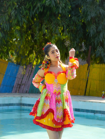 Model in bright multicolor Famameha boho mini dress with sweetheart bodice, bell sleeves, and ruffled hem, poolside front view.