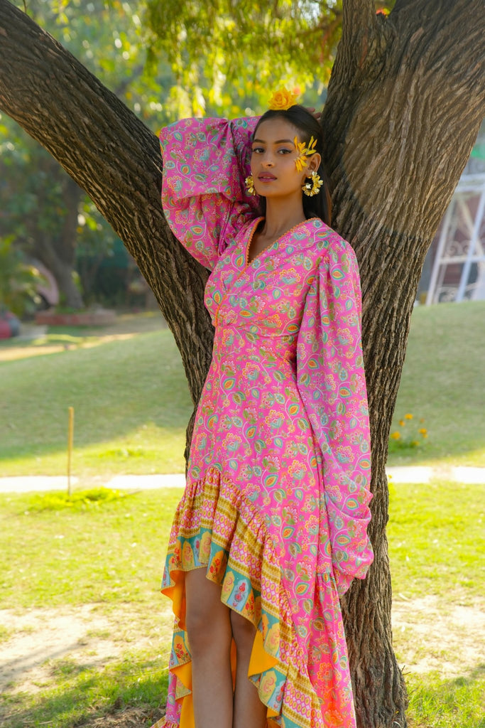 Front view of Famameha pink floral boho dress with bishop sleeves and asymmetric layered hem, model leaning on a tree.